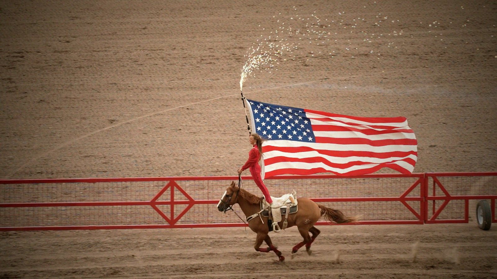 A rider carrying the American flag around a rodeo arena